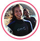 Profielfoto van reviewer, een jonge vrouw in wetsuit lachend op een strand.
