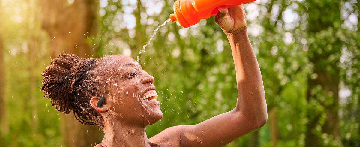 Vrouw die zich afkoelt door water over haar hoofd te gieten terwijl ze Philips sporthoofdtelefoon draagt in de buitenlucht